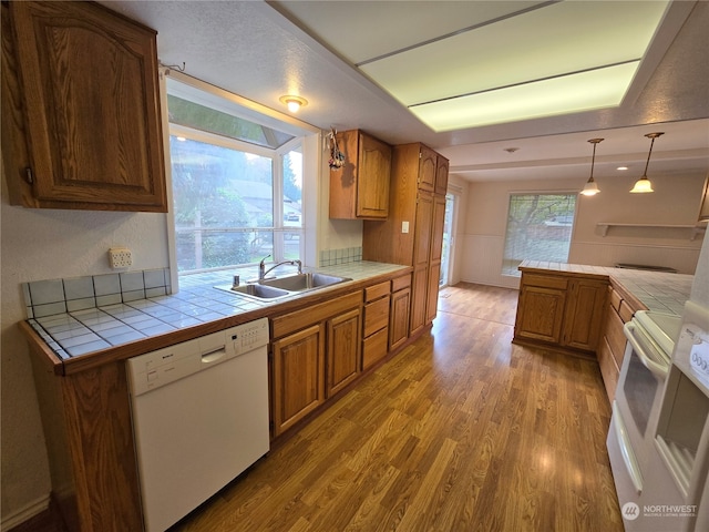 kitchen with hanging light fixtures, tile countertops, hardwood / wood-style flooring, sink, and white appliances