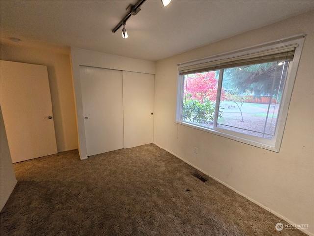 unfurnished bedroom featuring a closet, rail lighting, and carpet floors