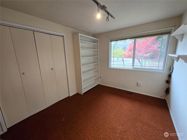 unfurnished bedroom with a closet, track lighting, and dark colored carpet