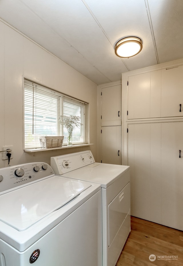 laundry area featuring washing machine and dryer, light wood-type flooring, and cabinets