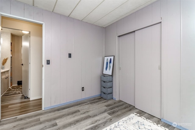 unfurnished bedroom with a closet, light wood-type flooring, and wood walls