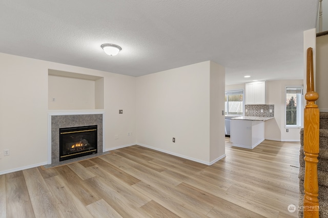 unfurnished living room with a tiled fireplace, a textured ceiling, and light hardwood / wood-style flooring