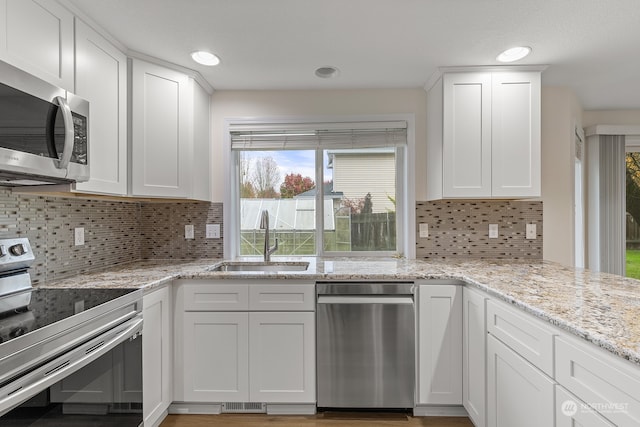 kitchen with light stone counters, stainless steel appliances, white cabinetry, backsplash, and sink