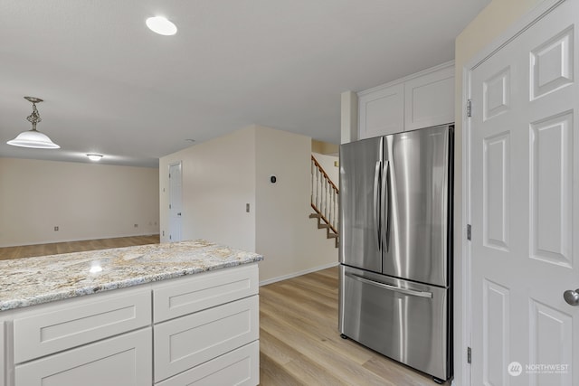 kitchen featuring light hardwood / wood-style floors, light stone counters, white cabinets, stainless steel refrigerator, and pendant lighting