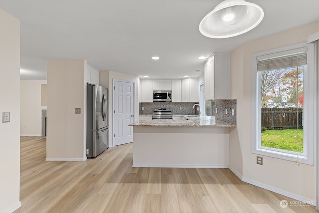 kitchen with light hardwood / wood-style floors, white cabinetry, kitchen peninsula, light stone counters, and appliances with stainless steel finishes