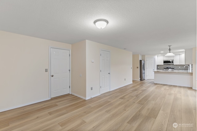 unfurnished living room with a textured ceiling, light hardwood / wood-style floors, and sink