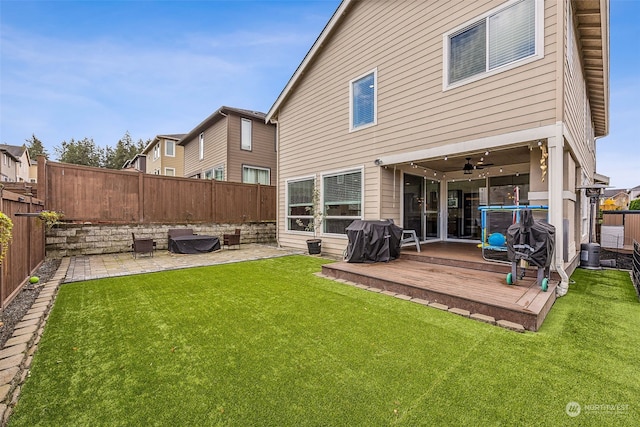 rear view of property featuring a yard, ceiling fan, a wooden deck, and a patio area