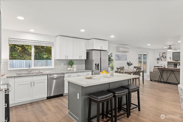 kitchen with stainless steel appliances, a wall mounted AC, white cabinets, and a healthy amount of sunlight