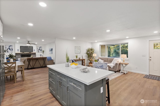 kitchen with light hardwood / wood-style floors, a breakfast bar area, gray cabinets, ceiling fan, and a kitchen island