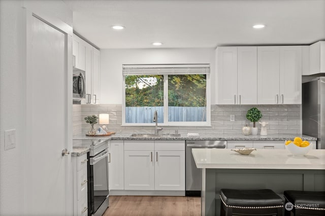 kitchen with tasteful backsplash, stainless steel appliances, sink, white cabinets, and light hardwood / wood-style flooring