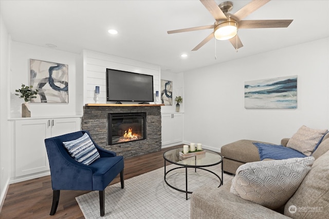 living room featuring dark wood-type flooring, a stone fireplace, and ceiling fan