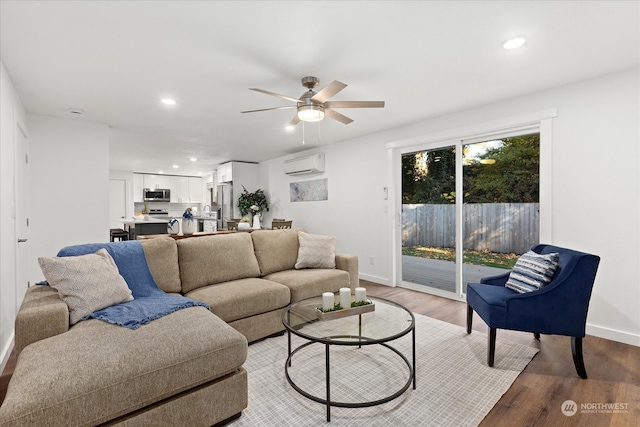 living room with a wall mounted AC, wood-type flooring, and ceiling fan