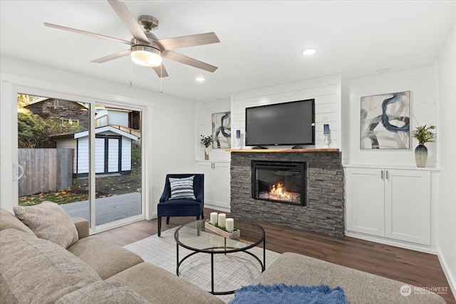 living room with ceiling fan, dark hardwood / wood-style floors, and a stone fireplace