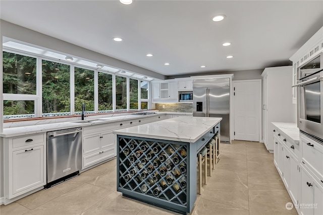 kitchen featuring built in appliances, white cabinetry, sink, a kitchen island, and light stone counters