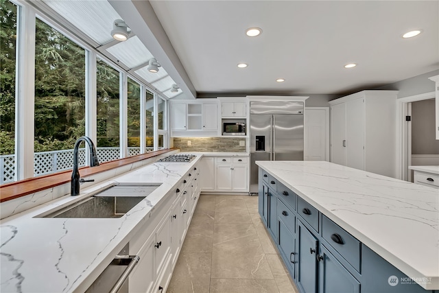 kitchen with sink, white cabinetry, blue cabinets, light stone counters, and built in appliances