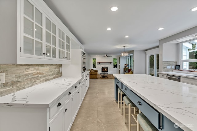 kitchen featuring white cabinets, backsplash, hanging light fixtures, and light stone counters