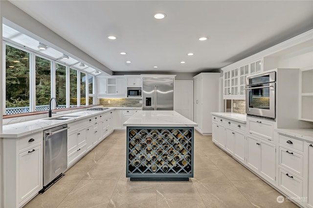 kitchen with light stone countertops, a center island, built in appliances, tasteful backsplash, and sink