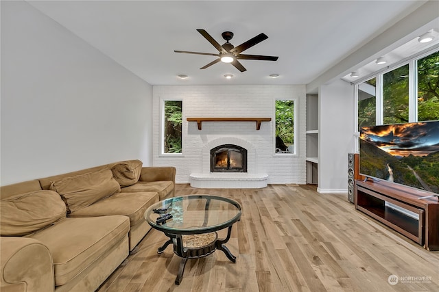 living room featuring ceiling fan, light hardwood / wood-style floors, brick wall, and a brick fireplace