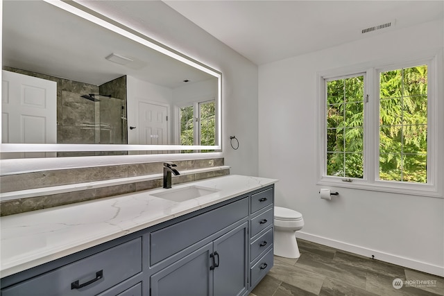 bathroom with vanity, toilet, a healthy amount of sunlight, and tiled shower