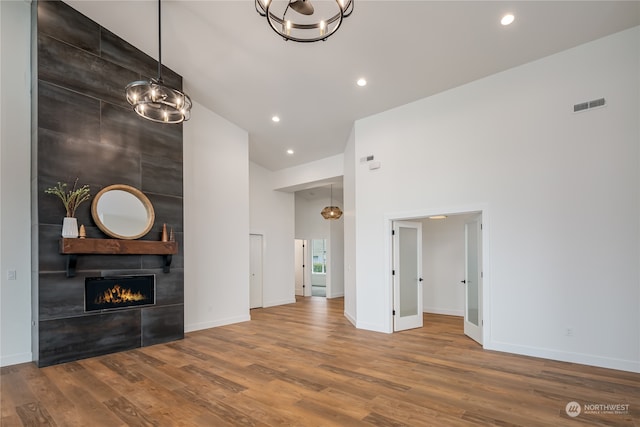 unfurnished living room with a tile fireplace, a notable chandelier, wood-type flooring, and high vaulted ceiling