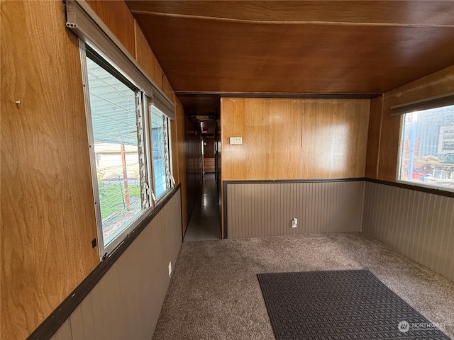 empty room featuring wood walls, wooden ceiling, and dark carpet