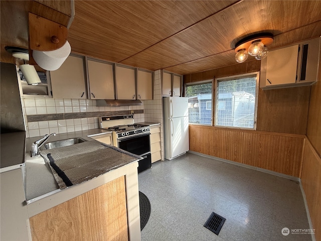 kitchen with wood ceiling, wood walls, black gas range oven, and white refrigerator