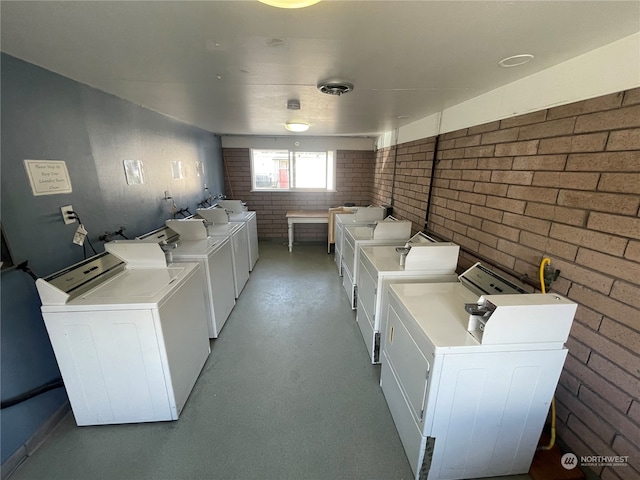 laundry area with brick wall and washer and clothes dryer