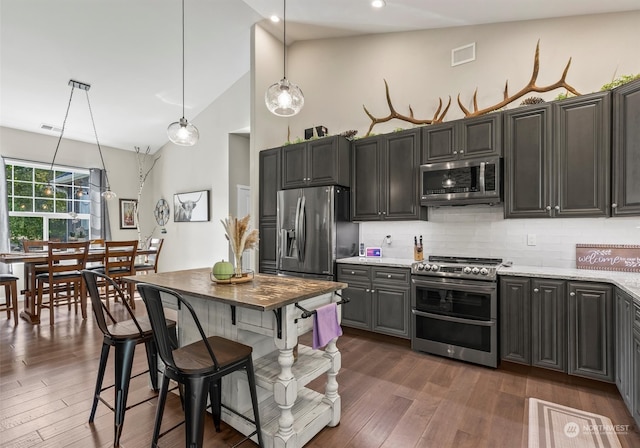 kitchen featuring dark wood-type flooring, high vaulted ceiling, decorative light fixtures, a breakfast bar, and appliances with stainless steel finishes