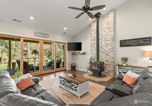 living room with ceiling fan, wood-type flooring, a wood stove, and high vaulted ceiling