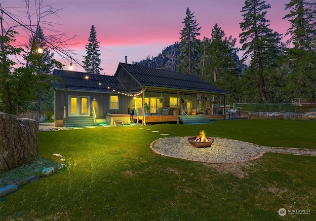 back house at dusk featuring a yard, a fire pit, and a deck