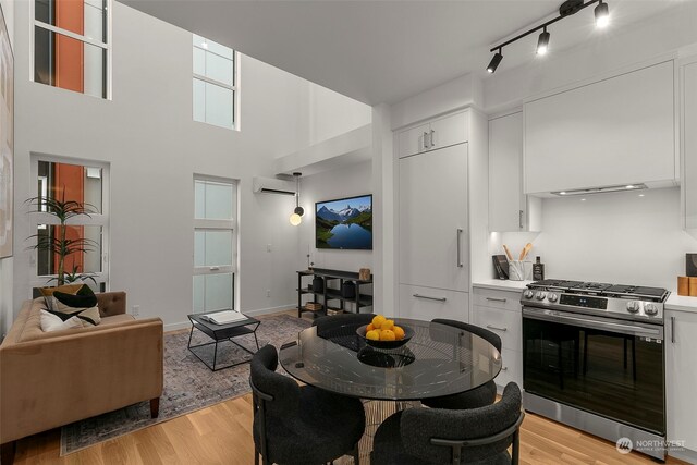 dining room with a wall unit AC, light hardwood / wood-style floors, and a high ceiling