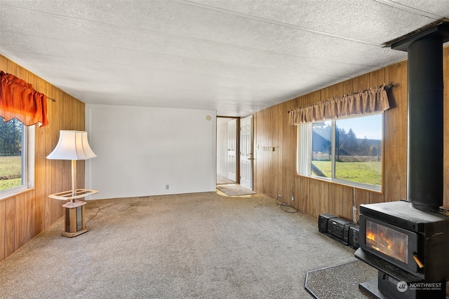 carpeted living room with wood walls, a textured ceiling, a wood stove, and vaulted ceiling