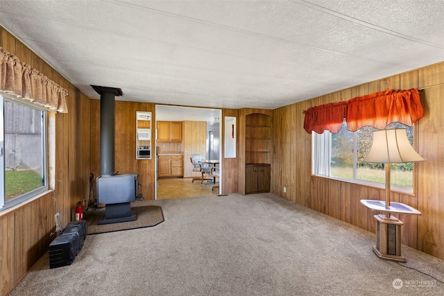 interior space with a textured ceiling, wood walls, a wood stove, and carpet floors