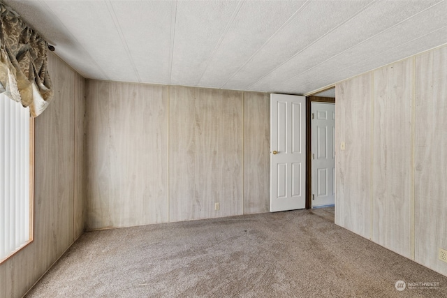 unfurnished room with a textured ceiling, wood walls, and light carpet