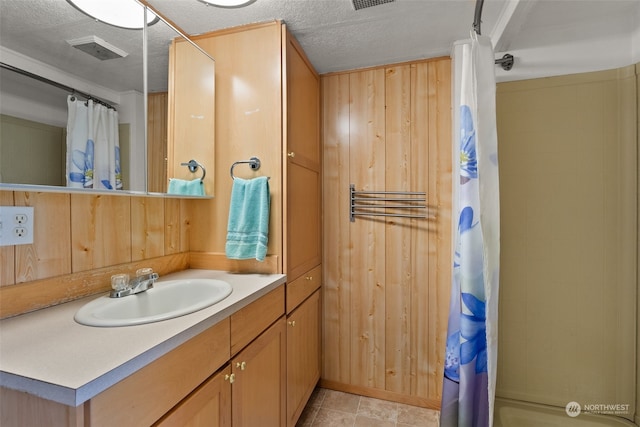 bathroom featuring a textured ceiling, vanity, wooden walls, and tile patterned floors