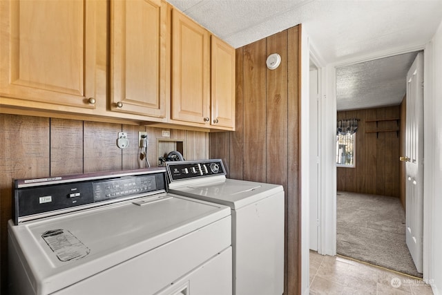 washroom featuring cabinets, a textured ceiling, washing machine and dryer, light colored carpet, and wooden walls