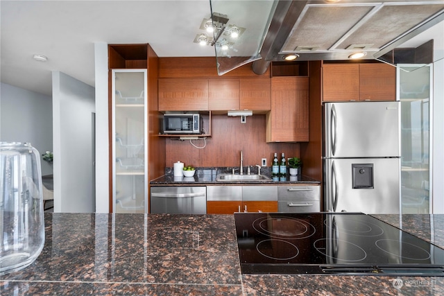 kitchen with appliances with stainless steel finishes, dark stone countertops, and sink