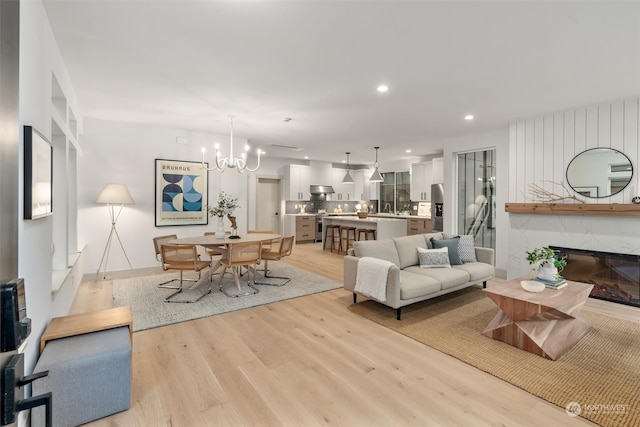 living room featuring an inviting chandelier, a high end fireplace, and light wood-type flooring