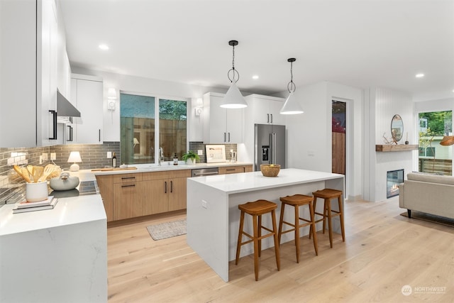 kitchen with white cabinets, tasteful backsplash, a kitchen island, stainless steel appliances, and decorative light fixtures