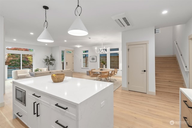 kitchen with a kitchen island, white cabinets, decorative light fixtures, and light hardwood / wood-style floors