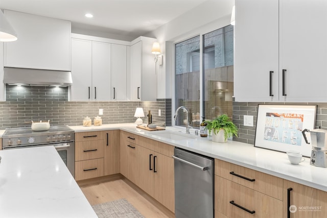 kitchen featuring light brown cabinets, white cabinets, exhaust hood, appliances with stainless steel finishes, and sink