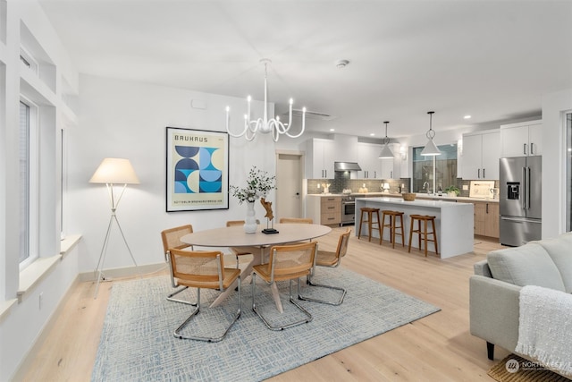 dining area with an inviting chandelier, sink, and light wood-type flooring