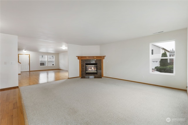 unfurnished living room featuring a high end fireplace, light hardwood / wood-style flooring, and plenty of natural light