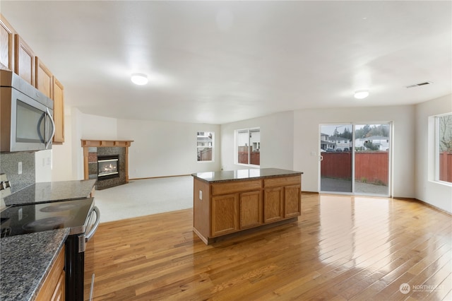 kitchen featuring light hardwood / wood-style flooring, a premium fireplace, electric range, and dark stone counters