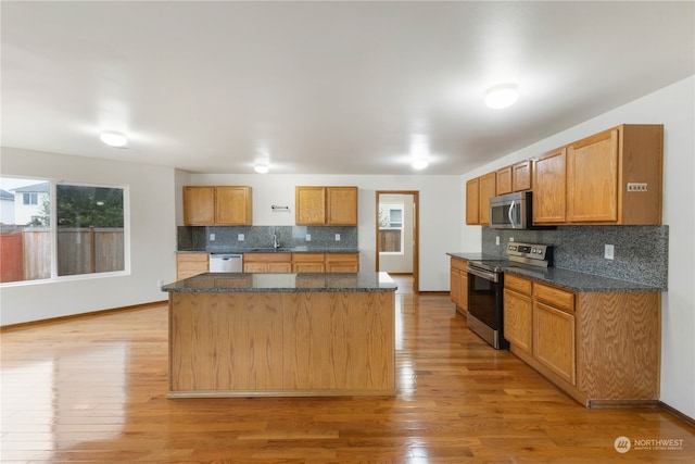 kitchen with appliances with stainless steel finishes, tasteful backsplash, light wood-type flooring, and a kitchen island