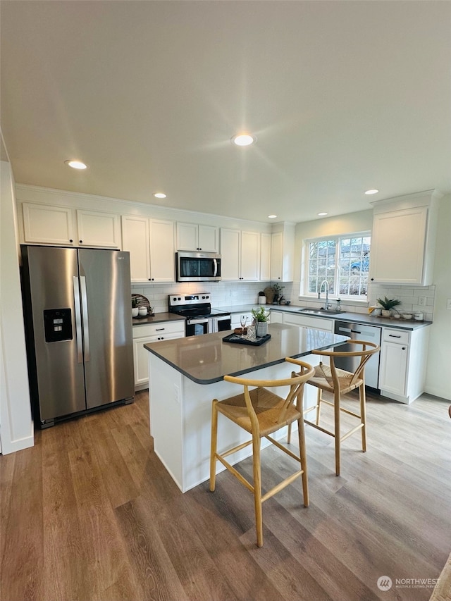 kitchen featuring hardwood / wood-style flooring, decorative backsplash, appliances with stainless steel finishes, a kitchen island, and white cabinetry