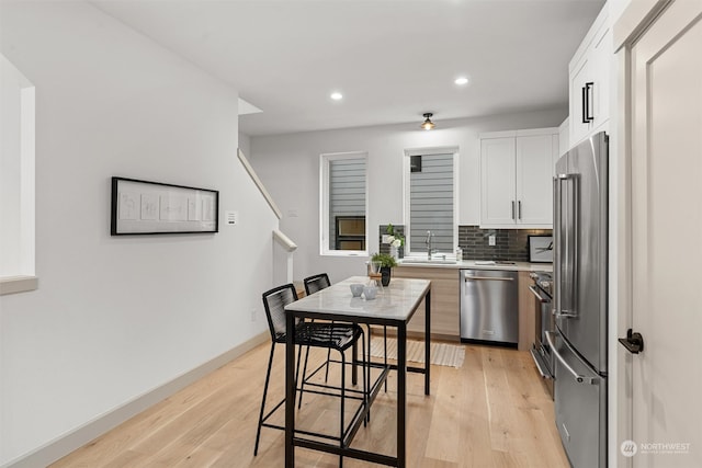 kitchen with white cabinets, backsplash, a breakfast bar, light wood-type flooring, and stainless steel appliances