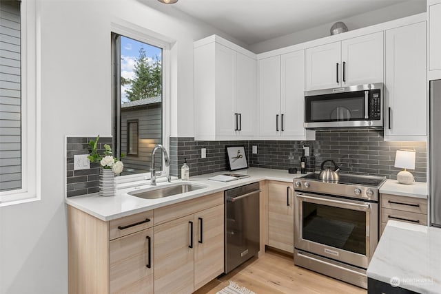 kitchen with appliances with stainless steel finishes, white cabinetry, light brown cabinetry, light wood-type flooring, and sink