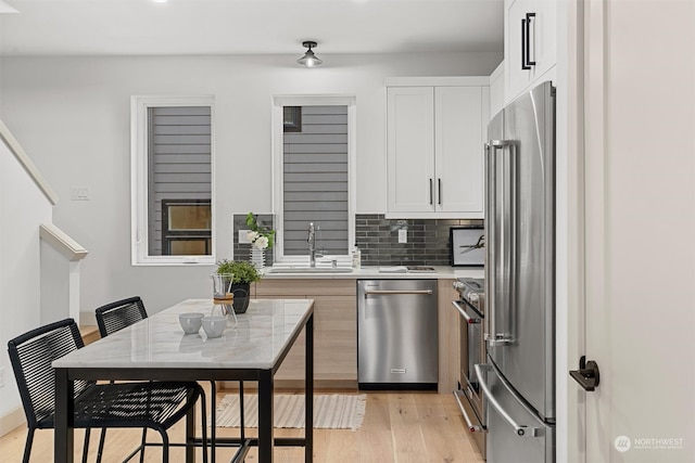 kitchen featuring tasteful backsplash, appliances with stainless steel finishes, sink, light hardwood / wood-style floors, and white cabinets