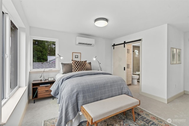 bedroom with ensuite bathroom, a barn door, a wall mounted air conditioner, and light colored carpet